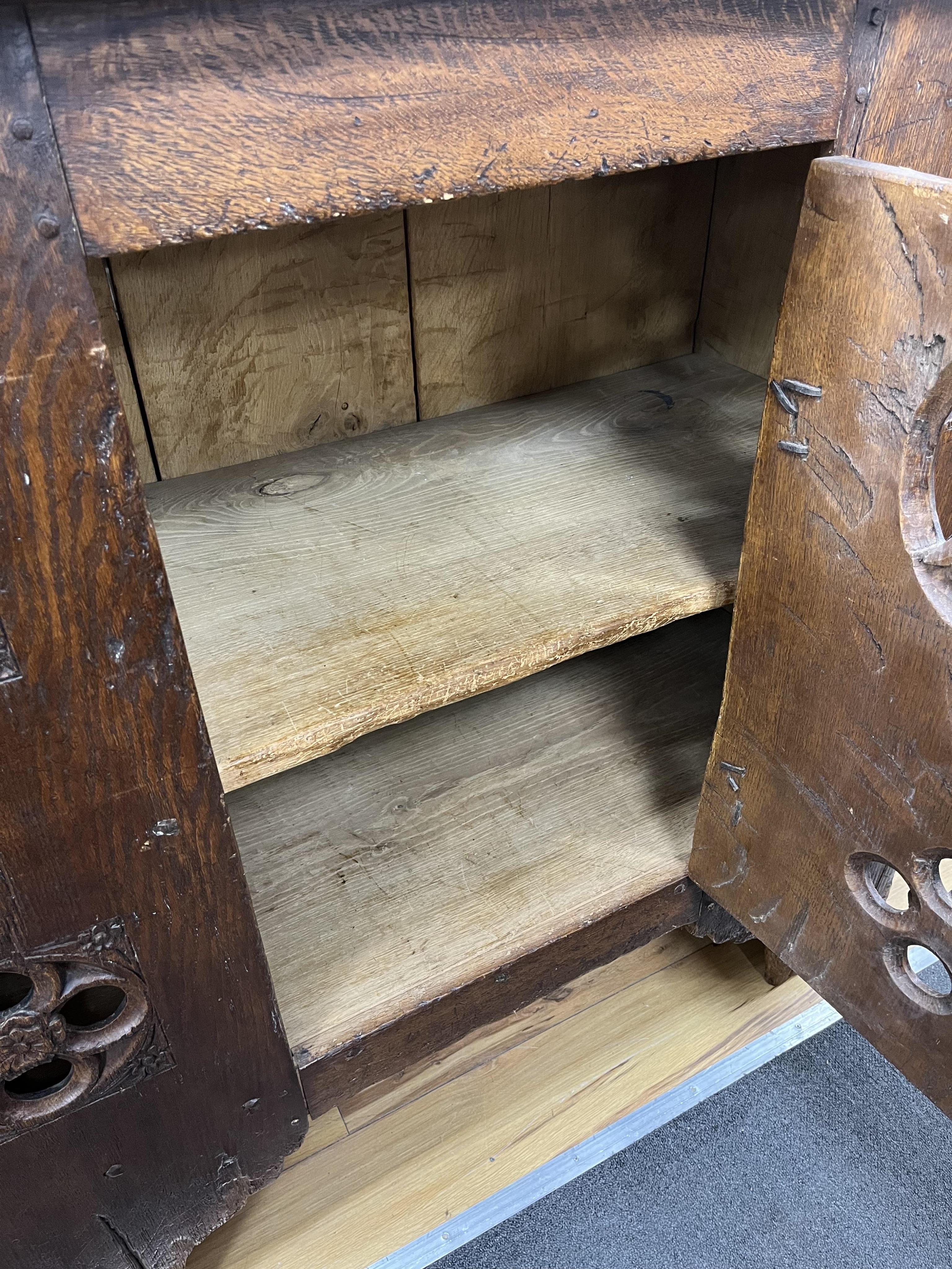 A boarded oak aumbry, in 16th century Tudor style, pierced and carved with armorial crests to the roundels, width 118cm, depth 55cm, height 114cm. Condition - fair to good, Provenance - made for Brede Place, Brede, Rye,